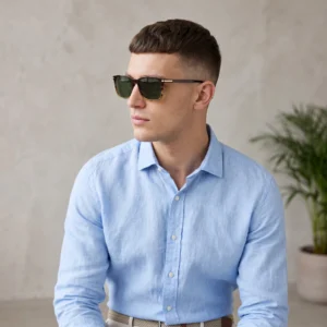 Side-profile of a man in a light blue button-down shirt wearing dark sunglasses indoors.