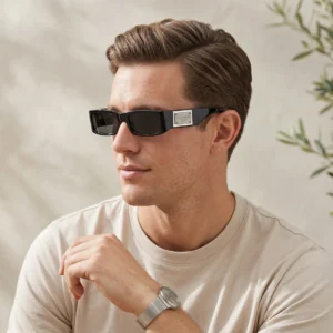 Man wearing black sunglasses and a silver watch, resting his chin on his hand in a beige shirt (side portrait).