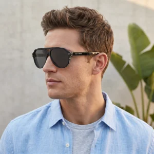 Man wearing black sunglasses with a Dolce & Gabbana logo on the temple, in a light blue shirt outdoors.
