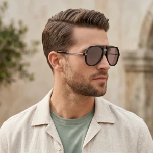 Close-up of a man wearing oversized black sunglasses and a beige linen shirt over a green T-shirt, outdoors with a blurred background.