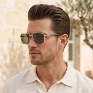 Close-up of a man wearing gold-framed sunglasses and a white polo shirt outdoors, with a light blurred background.