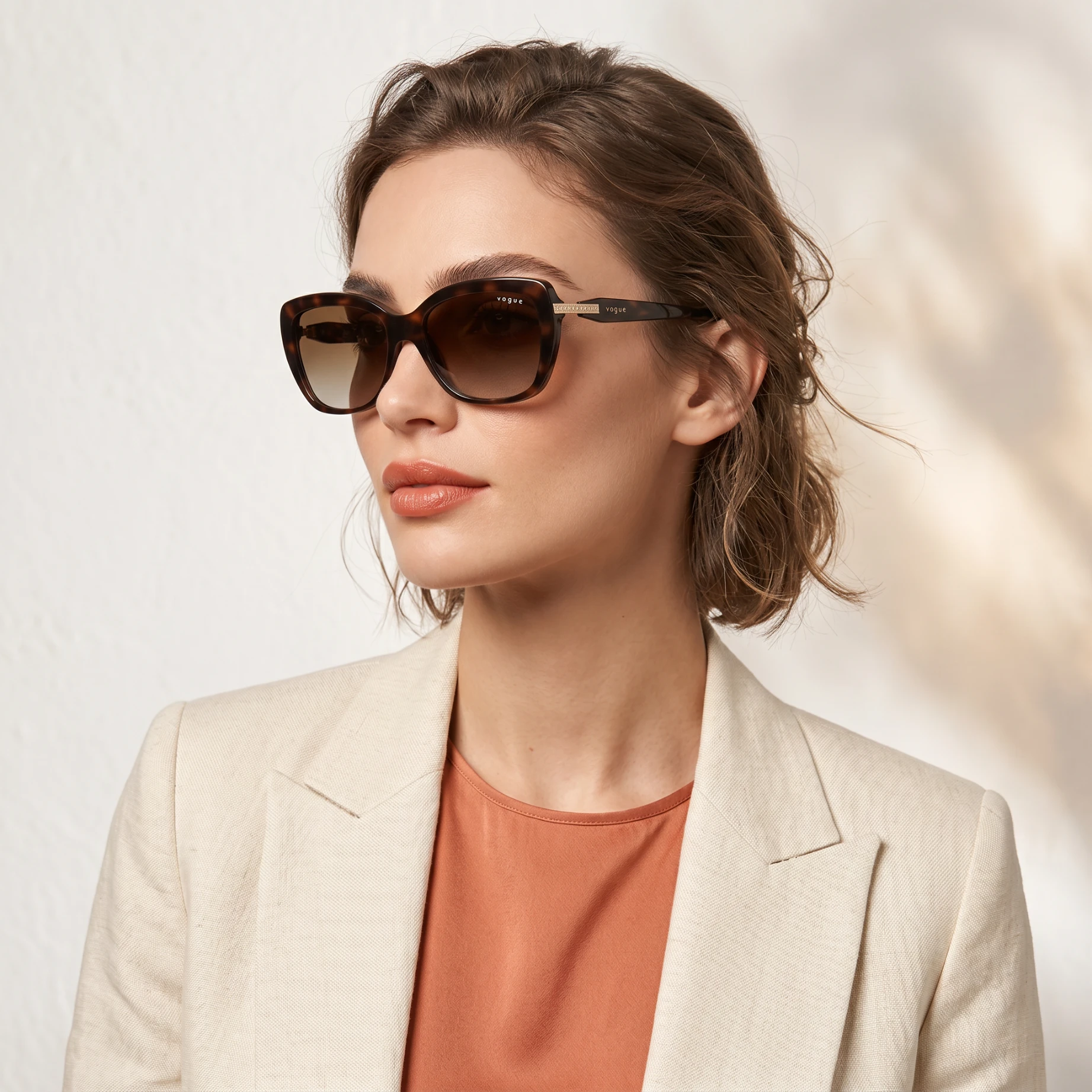 Woman wearing oversized tortoiseshell sunglasses, beige blazer, and peach top, profile view.
