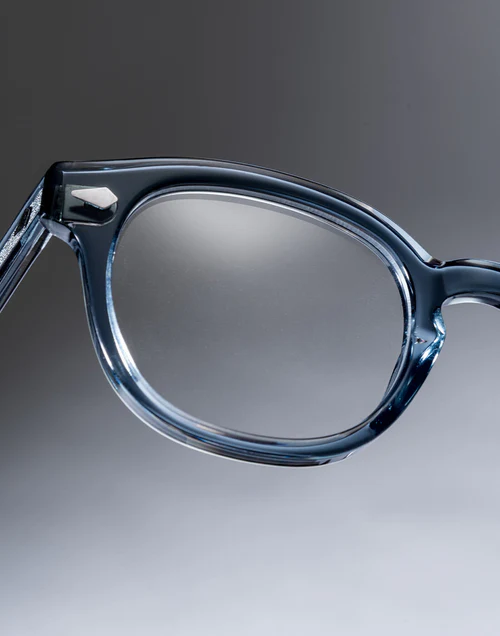 Close-up of blue translucent eyeglasses with rounded frame and reflective lenses on a gray gradient background.