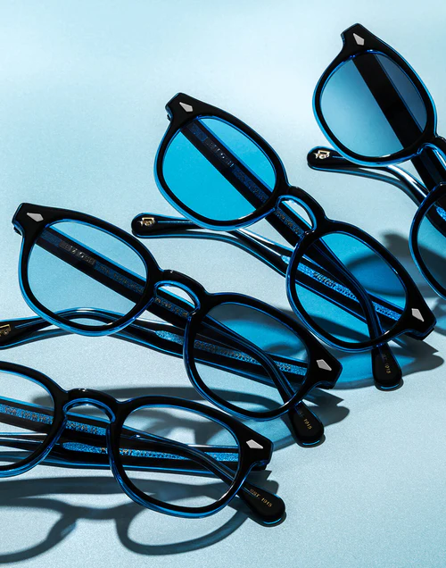Several blue round-framed eyeglasses arranged on a pale blue background with shadows.