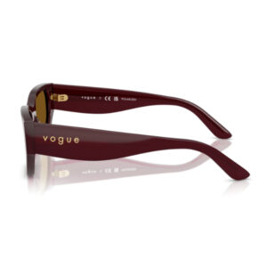 Side view of burgundy Vogue sunglasses with gold logo on the temple, reflected on a white surface.